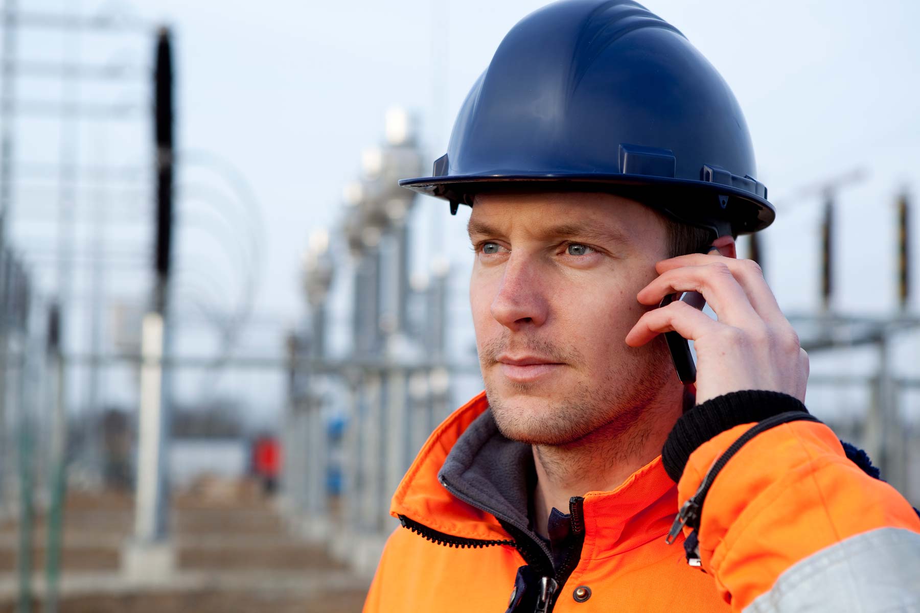 Man in hard hat and safety gear on phone at electric power plant
