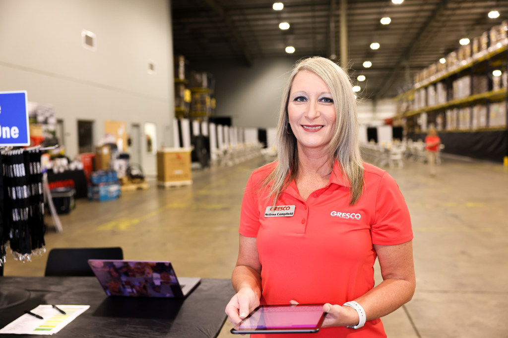 female gresco employee smiling in warehouse, holding tablet